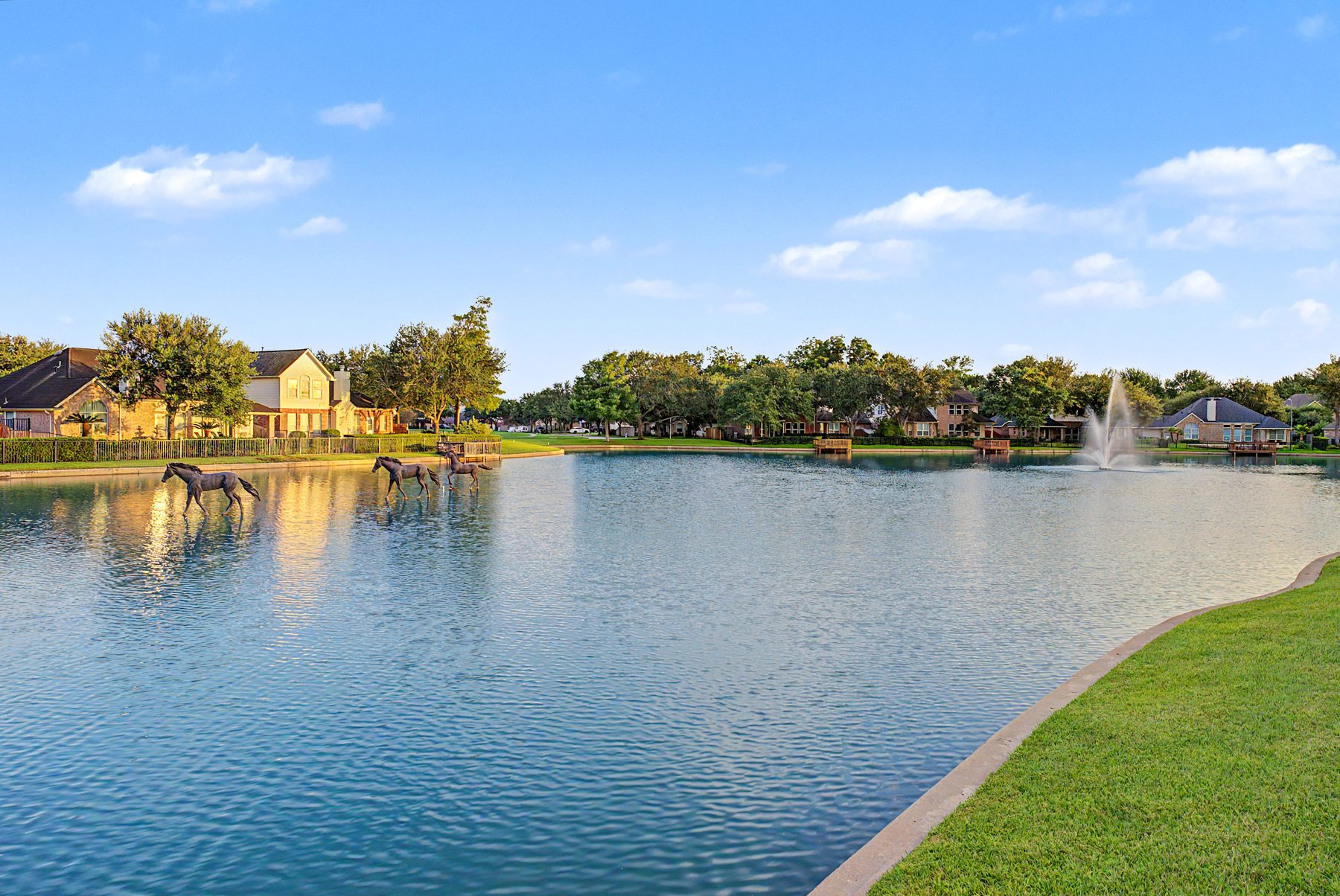 Bronze horse sculptures standing in the lake at Anderson Springs in Sienna, Missouri City TX, with fountain and homes behind