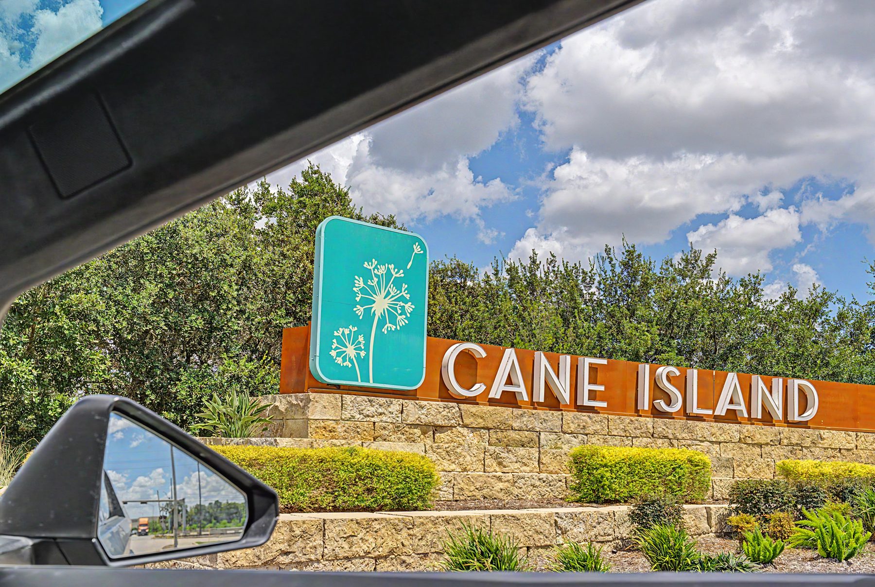 Cane Island monument sign on a limestone wall framed by a live oak at the community entrance in Katy