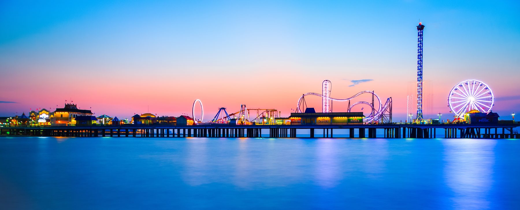 Galveston Island Historic Pleasure Pier lit up at blue hour above calm Gulf water