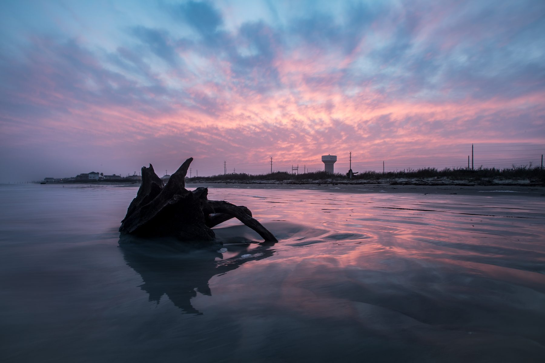 Jamaica Beach water tower on the horizon at sunset with driftwood on the wet sand