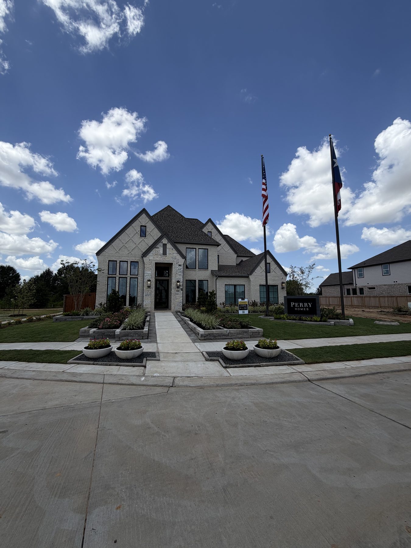 Brick and stone two-story model home with flagpoles at Lakes of Cane Island in Katy